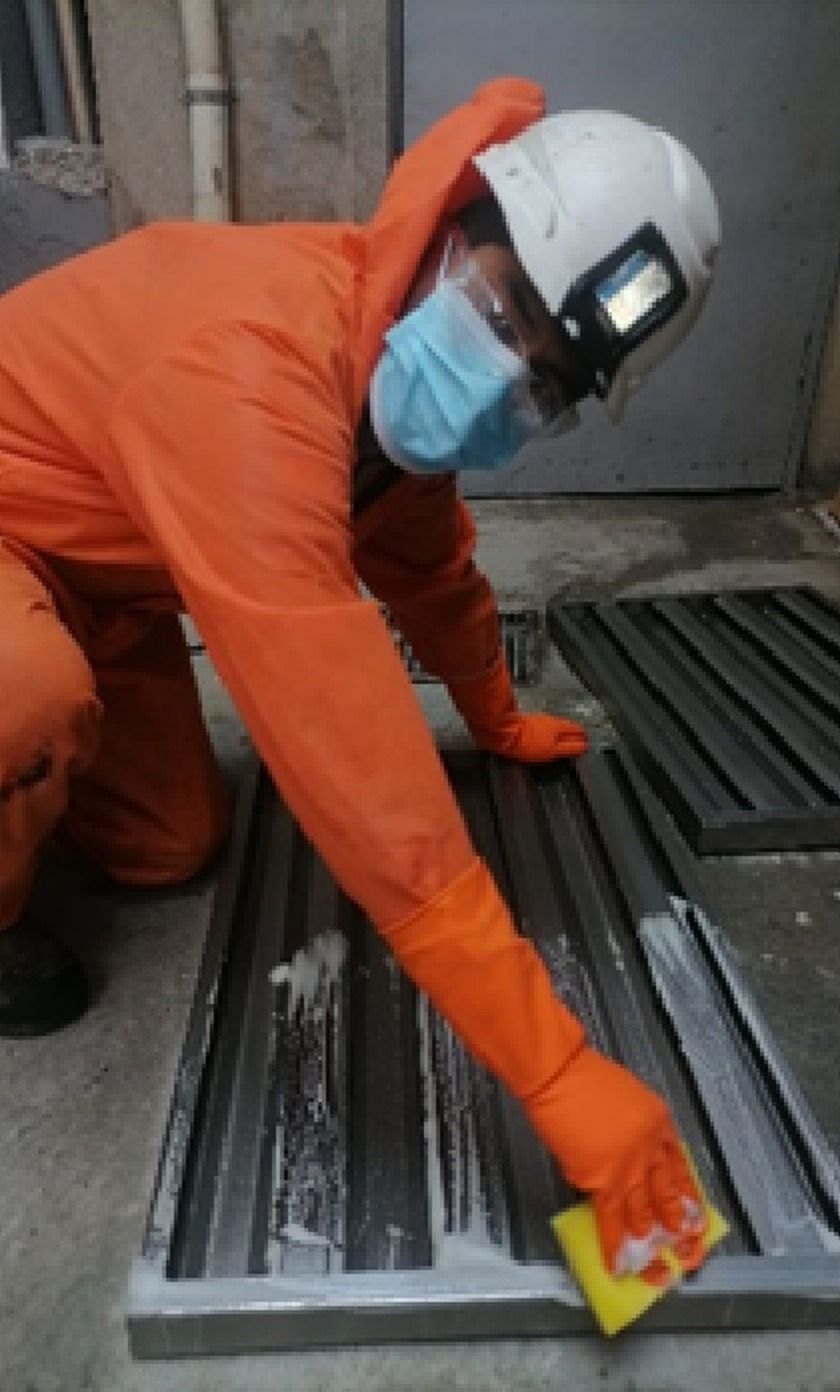 Técnico con traje naranja y casco limpiando un filtro de campana