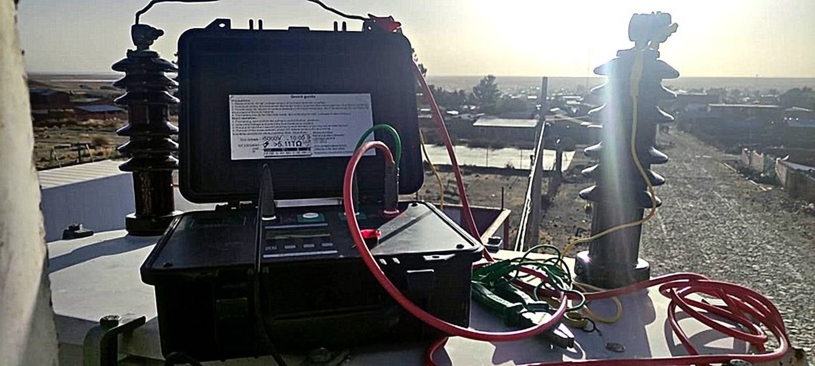 Maletín con equipo de medición y cables rojos, junto a aisladores
