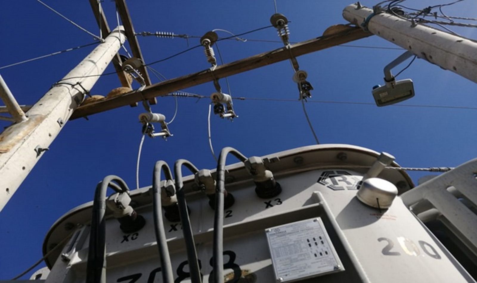 Transformador en un poste, visto desde abajo, con cables y aisladores